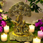 Antique brass Radha Krishna idol under tree, ideal for home decor and spiritual gifting, surrounded by candles and flowers.