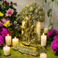 Antique finish brass Radha Krishna idol under tree with candles and flowers for spiritual home decor.